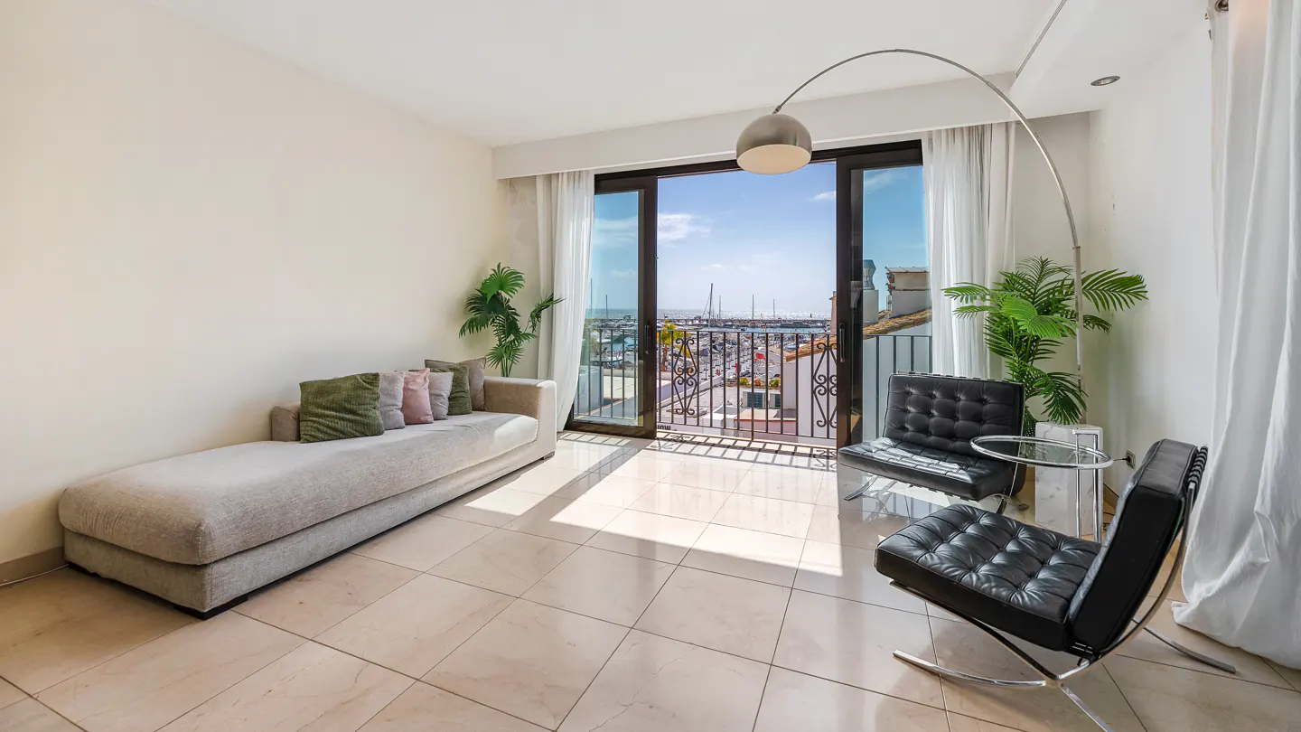 Bright living room with a chaise lounge, black chairs, and a balcony overlooking a marina.