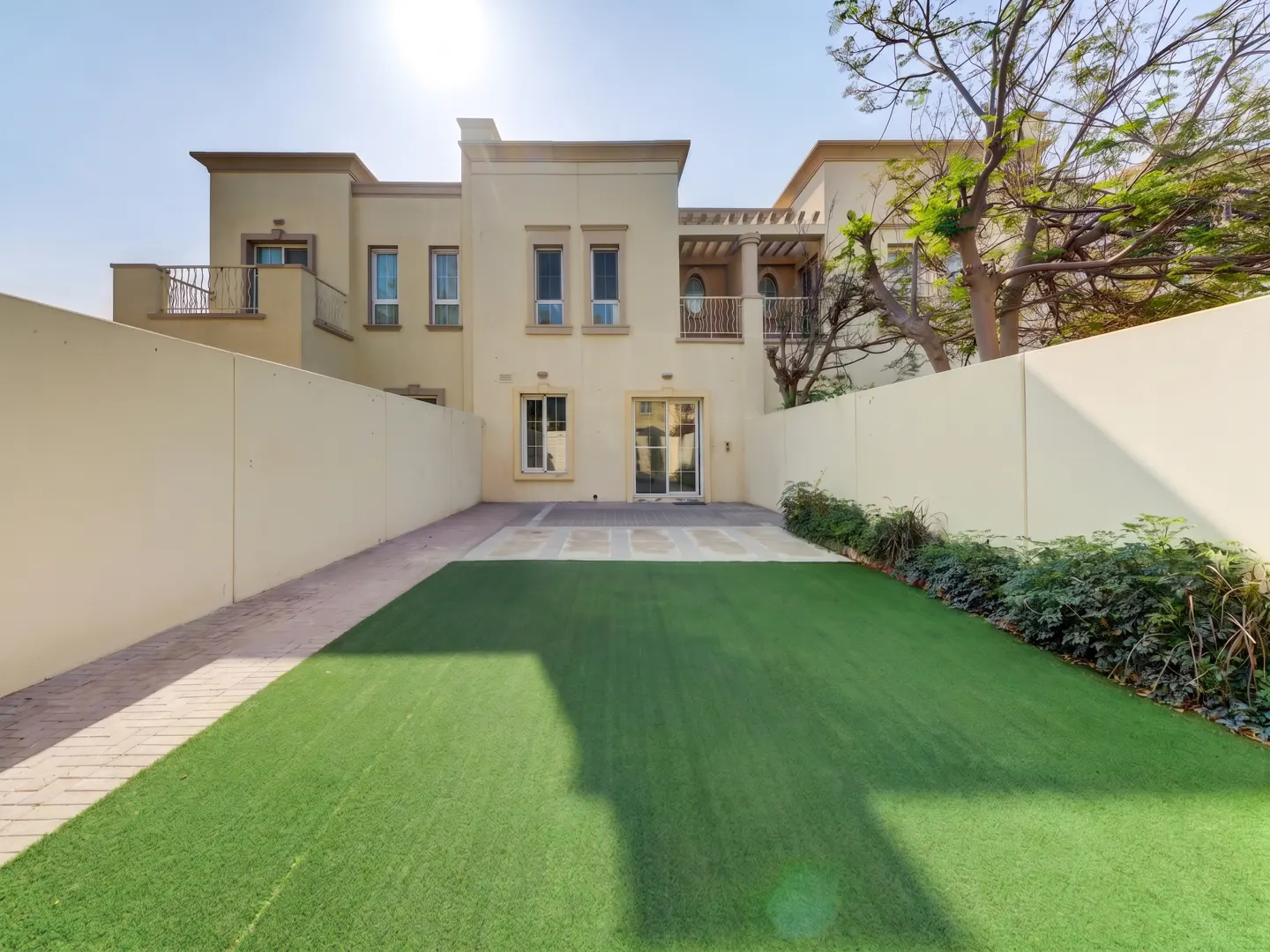 Backyard view of a two-story beige house with a green lawn and beige walls on a sunny day.