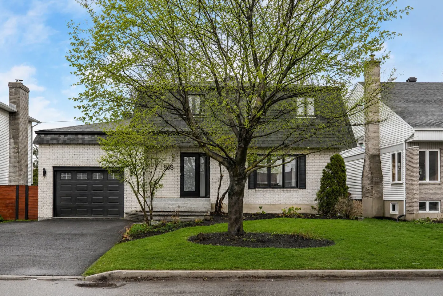 Two-story white brick house with black trim, a dark gray roof, and a large tree in the front yard.