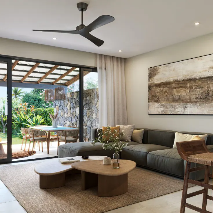Living room with a gray sofa, wooden coffee tables, and a ceiling fan. Outside, a patio with a dining table is visible.