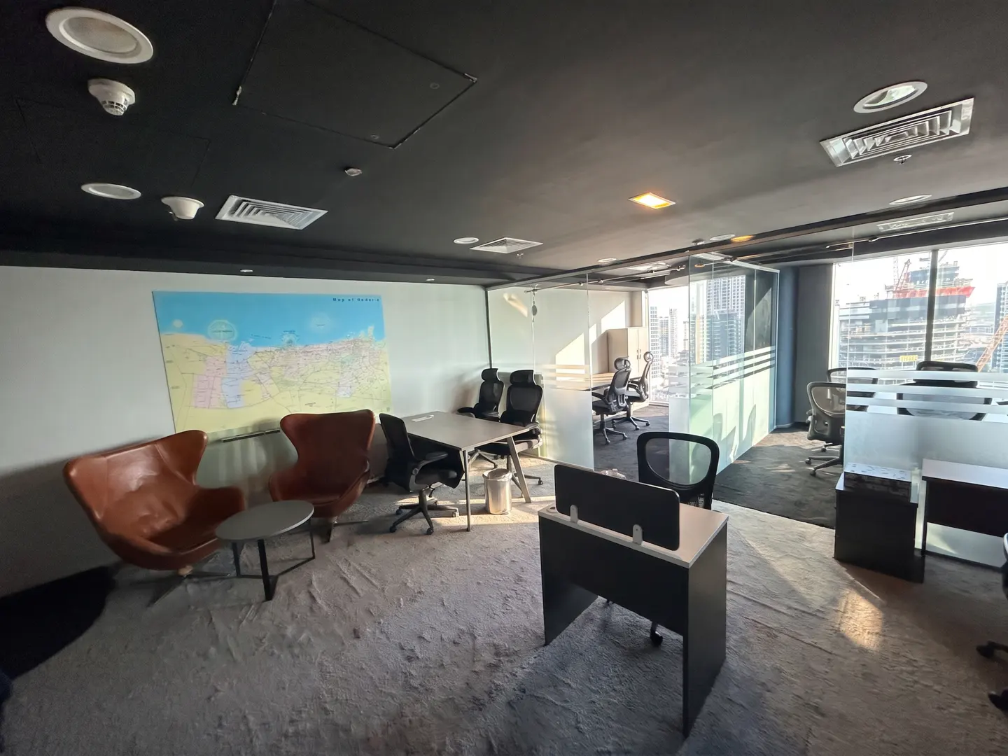 A modern office space with brown chairs, desks, and a map on the wall. Large windows offer a city view.