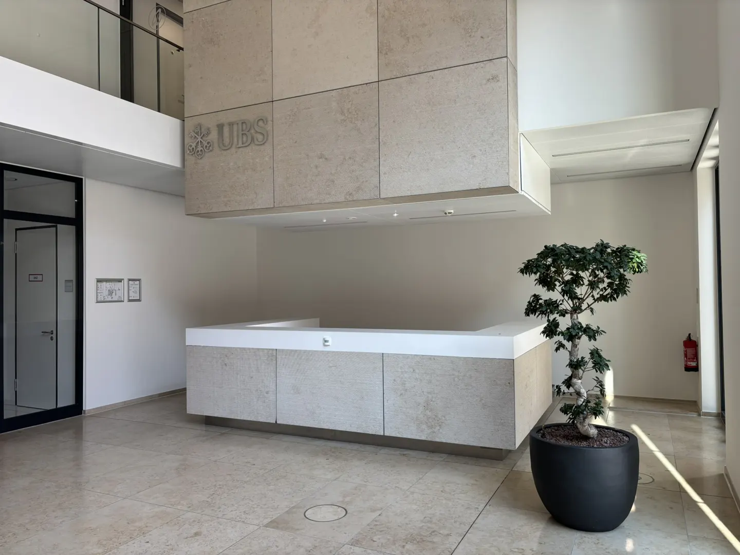 UBS office lobby with a stone reception desk, a bonsai tree in a black pot, and the UBS logo on the wall.