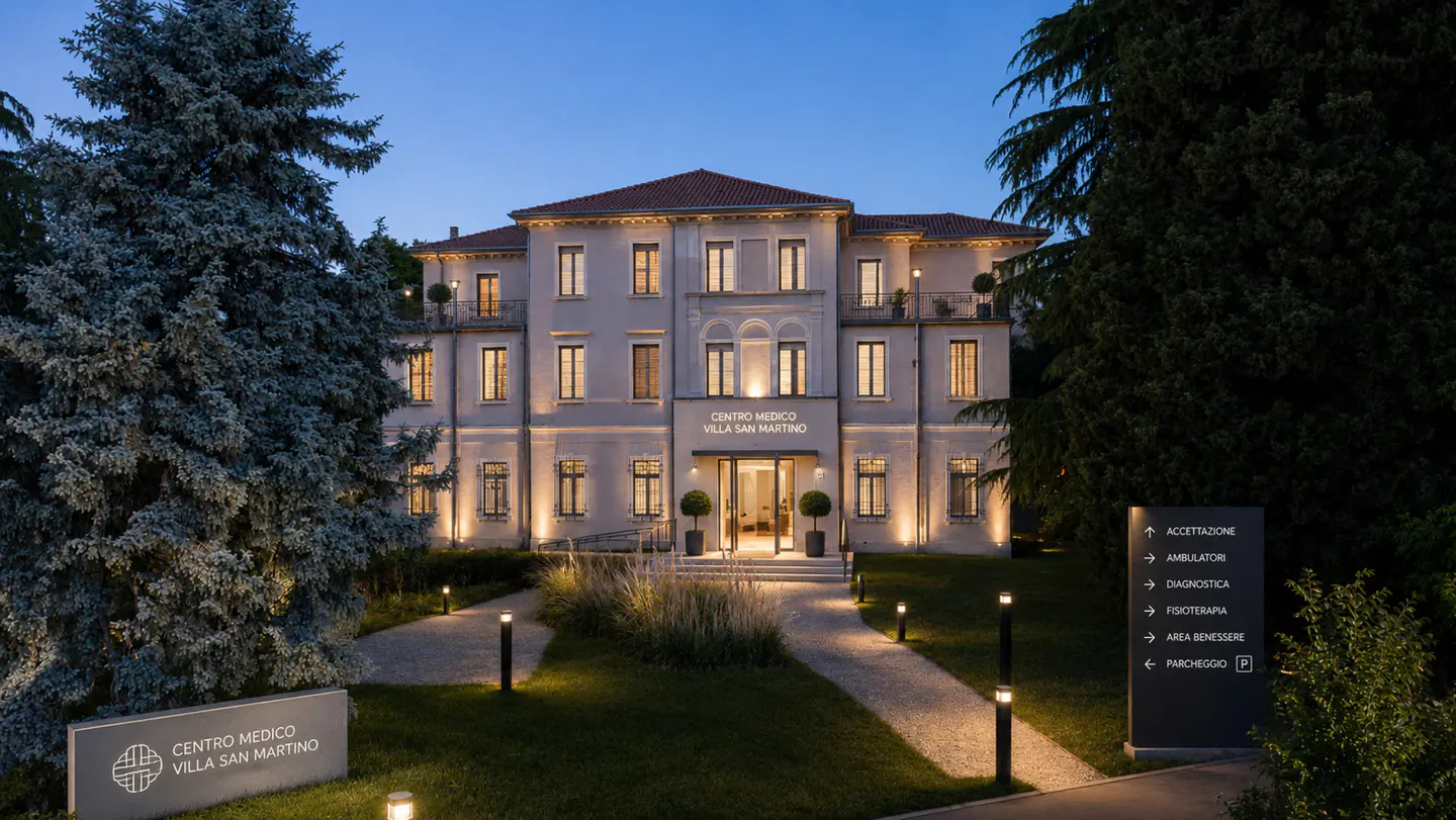 Exterior of Centro Medico Villa San Martino at dusk, with lit windows and pathways. Signage and landscaping visible.