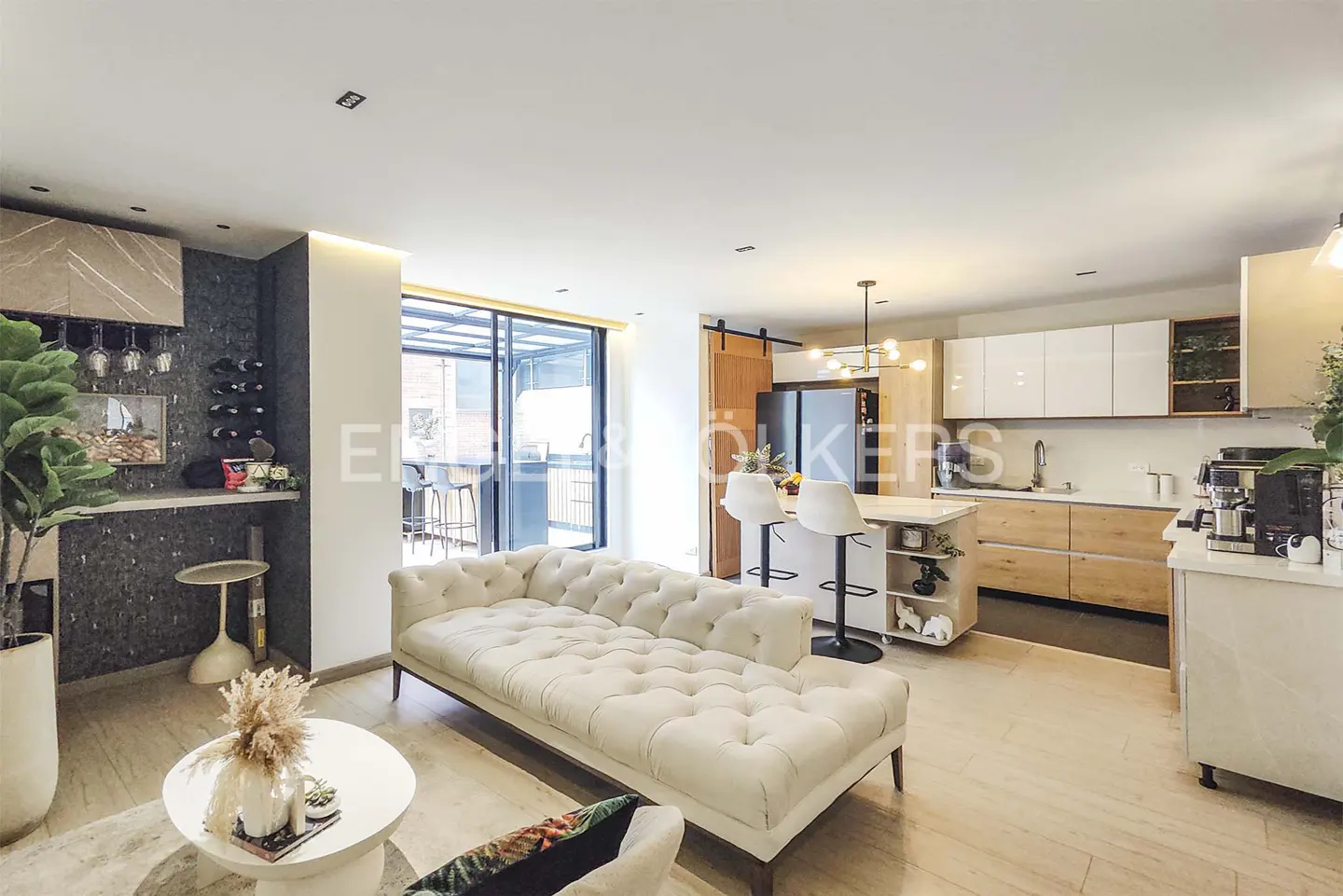 Open-concept living space with a white sofa, kitchen island with stools, and a bar area with wine storage.