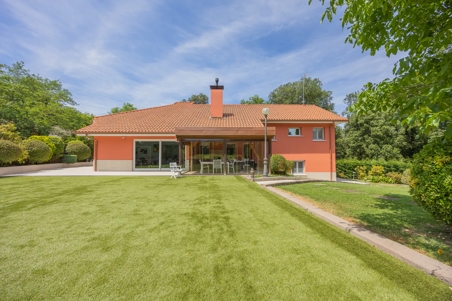 Orange house with a tiled roof, glass-enclosed patio, and a large, well-manicured green lawn under a bright blue sky.