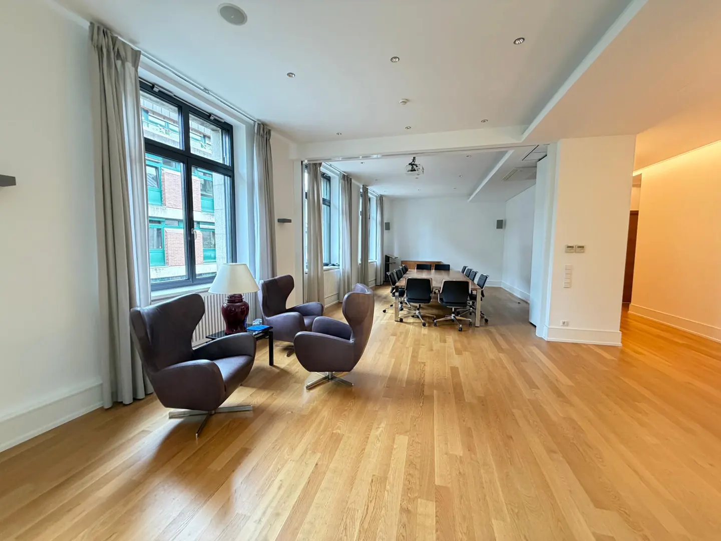 A bright, open office space with hardwood floors, purple chairs, and a conference table with black chairs. Natural light streams through large windows.