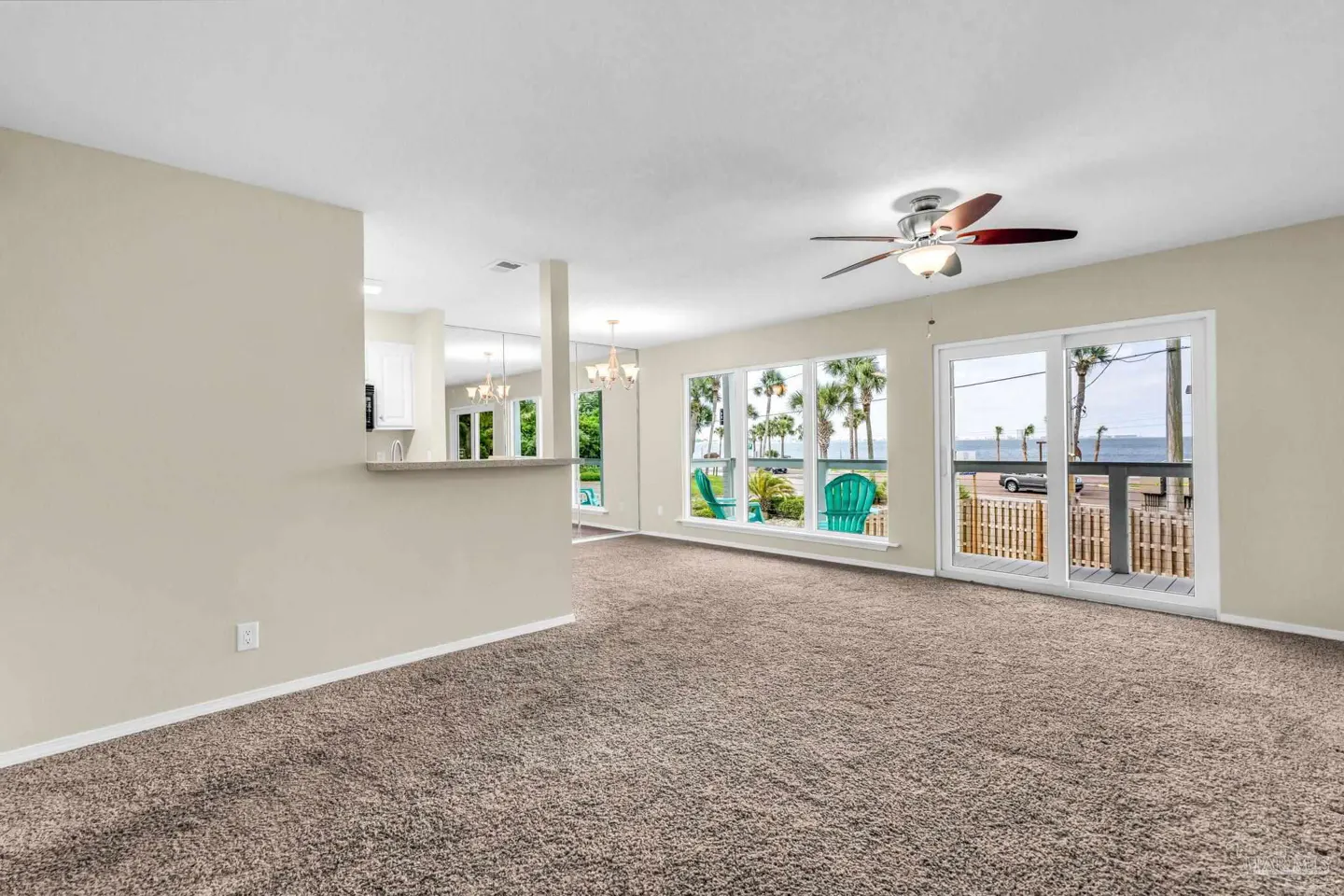 Spacious living room with beige walls, brown carpet, ceiling fan, and sliding glass doors overlooking a waterfront view.