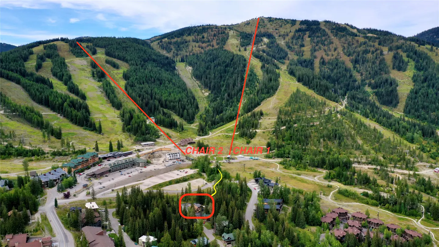 Aerial view of a ski resort with green slopes, chairlifts marked in red, and buildings at the base.