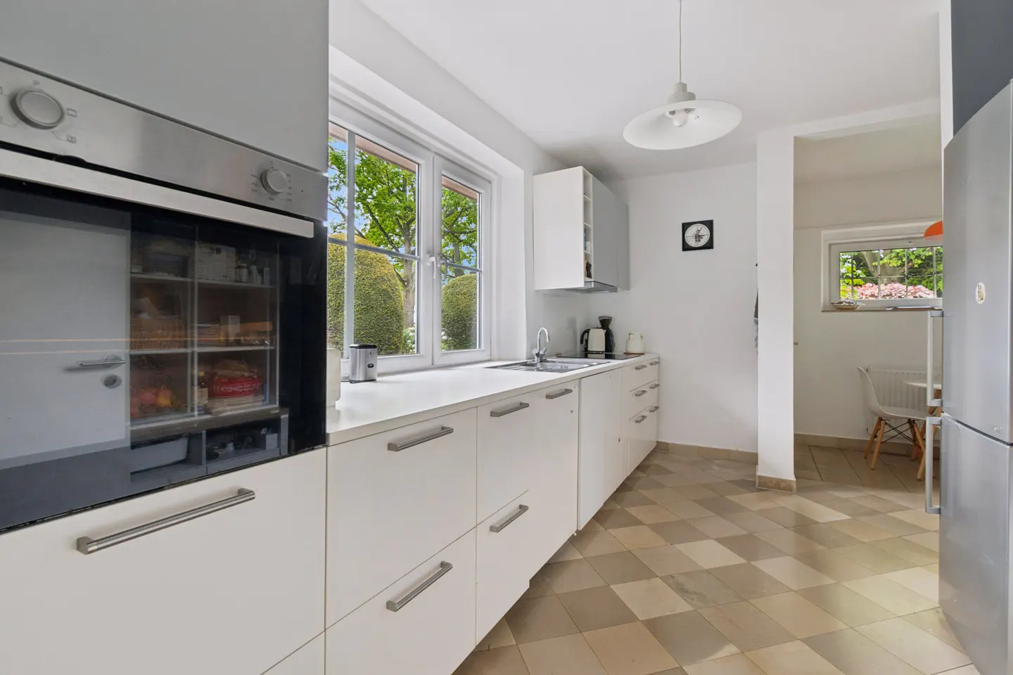 Modern kitchen with white cabinets, stainless steel oven, checkered tile floor, and a view into a small dining area.