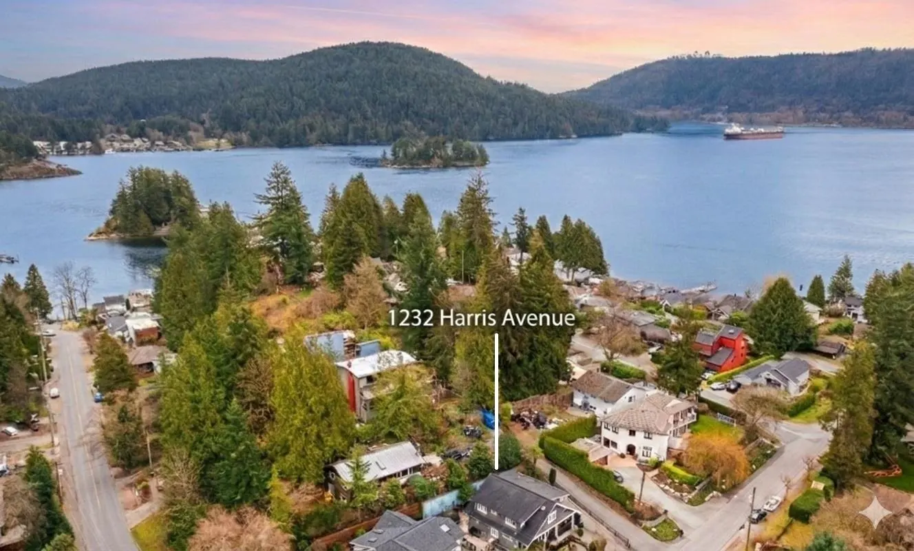 Aerial view of 1232 Harris Avenue, a house nestled among trees near a lake with mountains in the background.