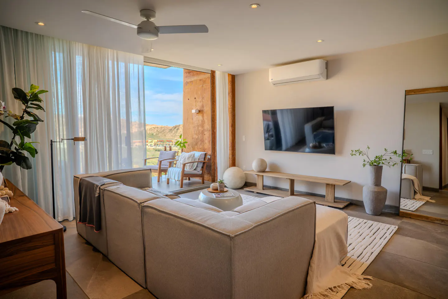 Living room with a gray sectional sofa, TV, and a view of the desert through a sliding glass door.
