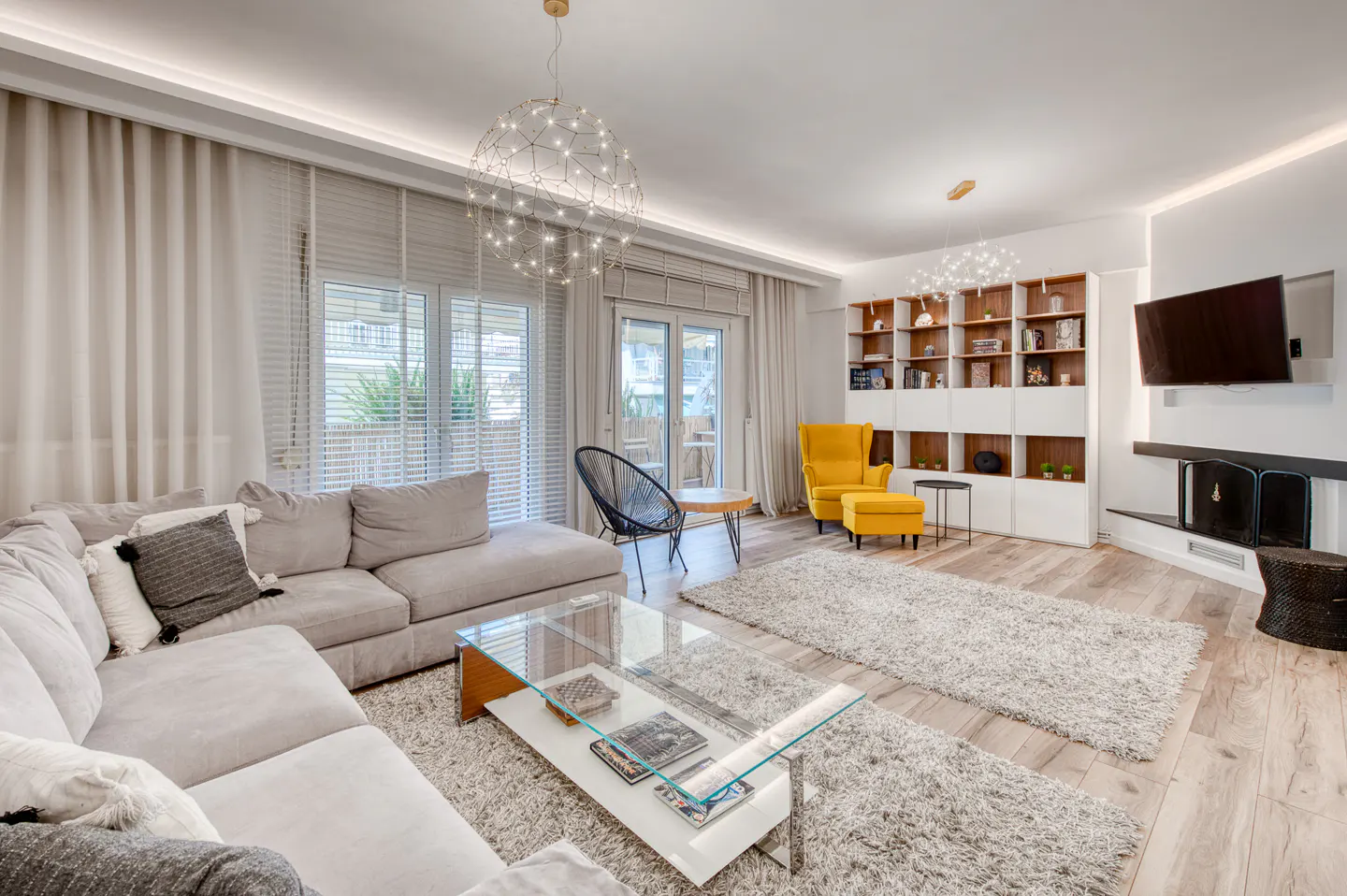 Modern living room with a grey sectional sofa, glass coffee table, yellow armchair, fireplace, and built-in shelving.