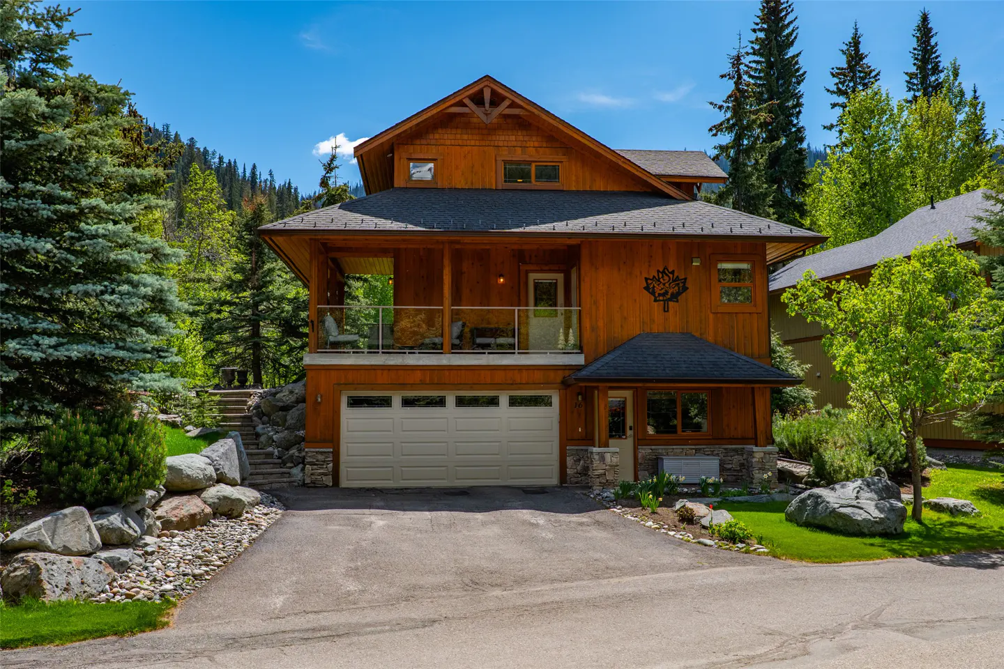 Two-story wood home with a white garage door and a balcony with glass railings. A maple leaf decoration is on the side of the house.