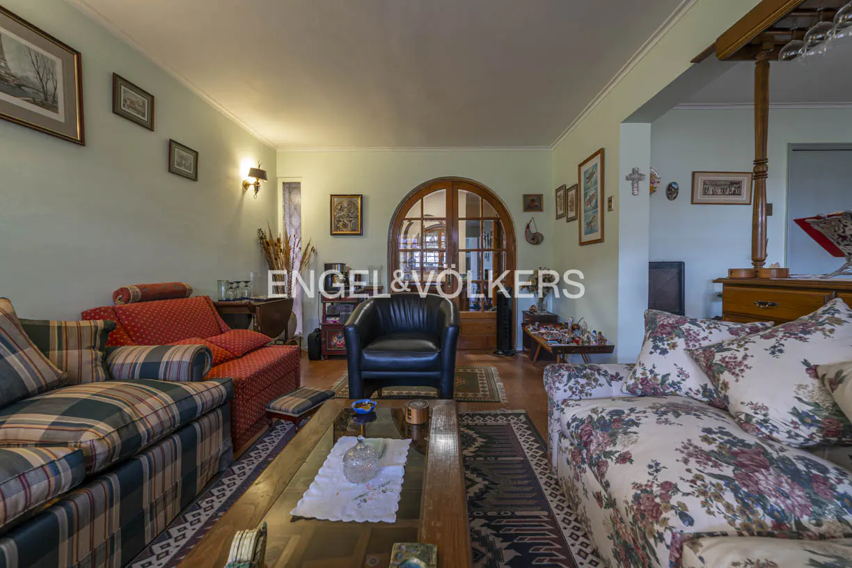 Living room with sofas, a black leather chair, and a wooden coffee table on a patterned rug. Arched doorway in the background.