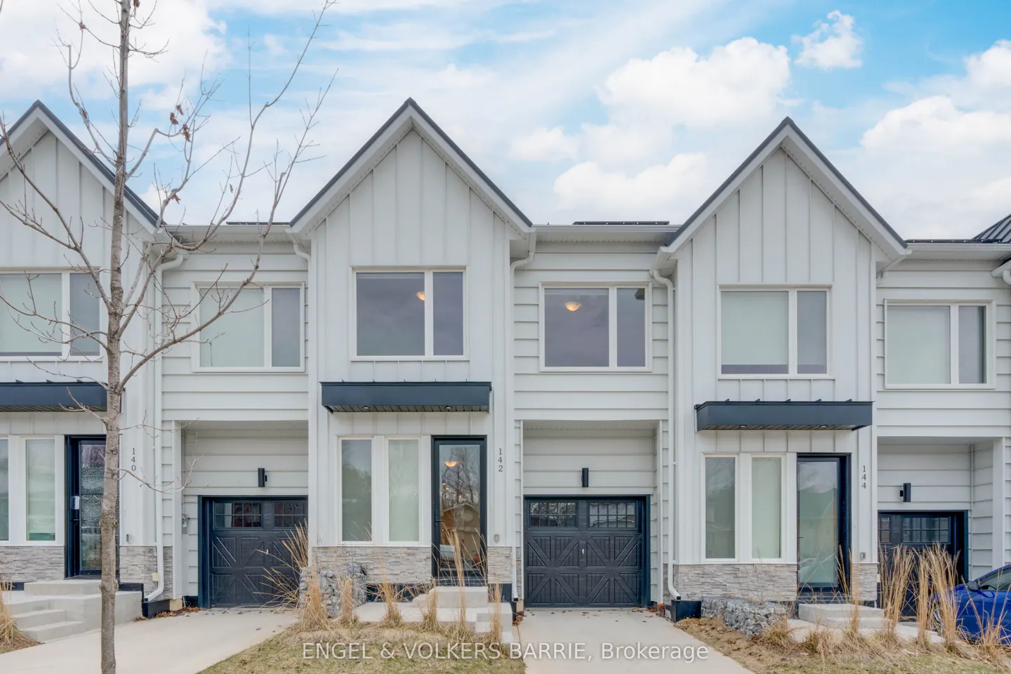 Exterior view of three modern, white townhouses with black garage doors under a cloudy sky.