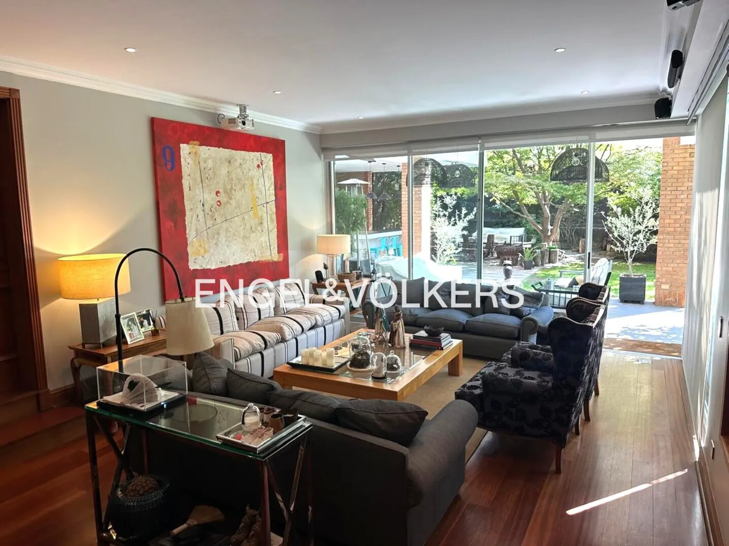 A spacious living room with hardwood floors, sofas, a coffee table, and a large window overlooking a backyard with a pool.