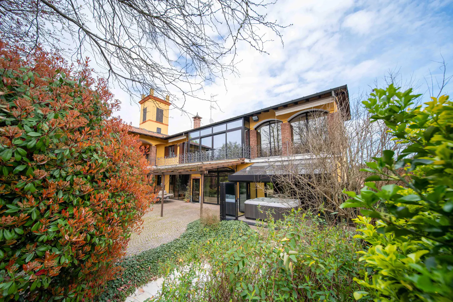 Exterior view of a yellow two-story house with a tower, a patio, and a hot tub.