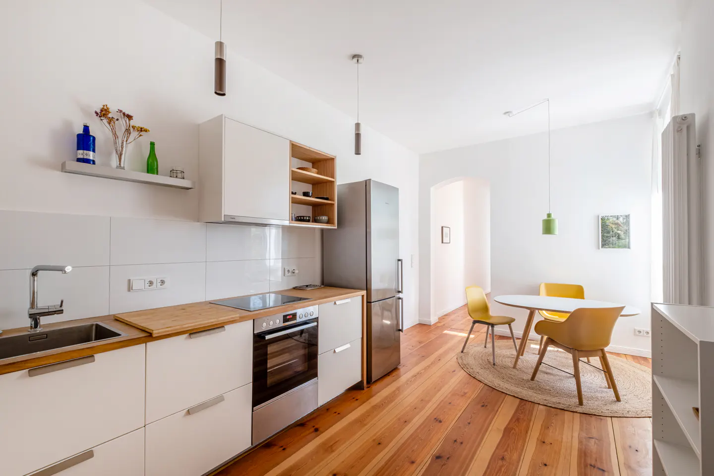 Bright, modern kitchen with white cabinets, wood countertops, stainless steel appliances, and a dining area with yellow chairs.