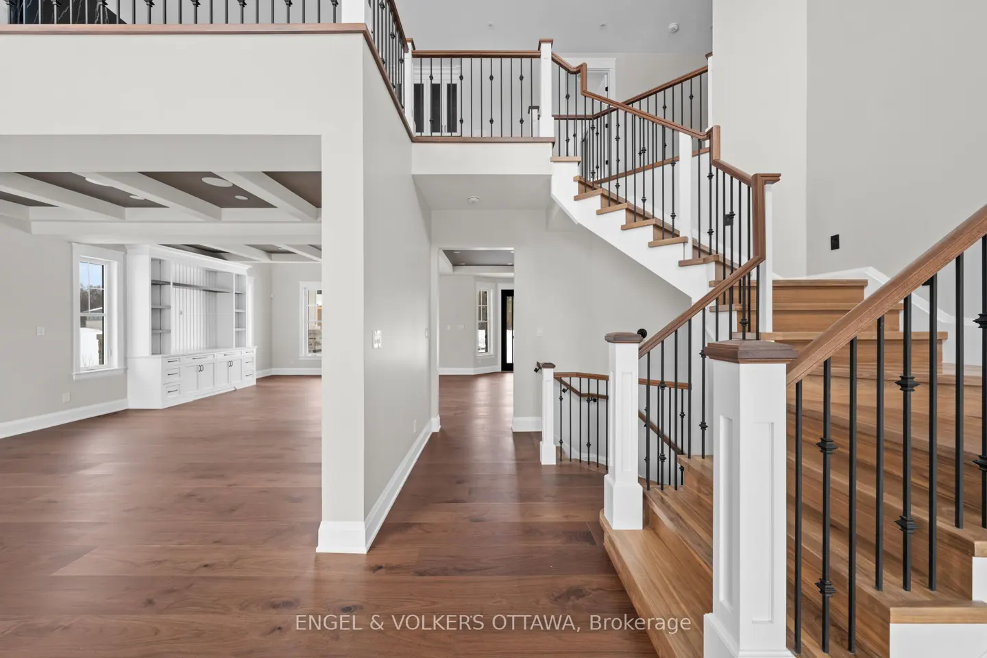 Interior view of a home's foyer with wood floors, a staircase with black iron railings, and an open-concept living area.