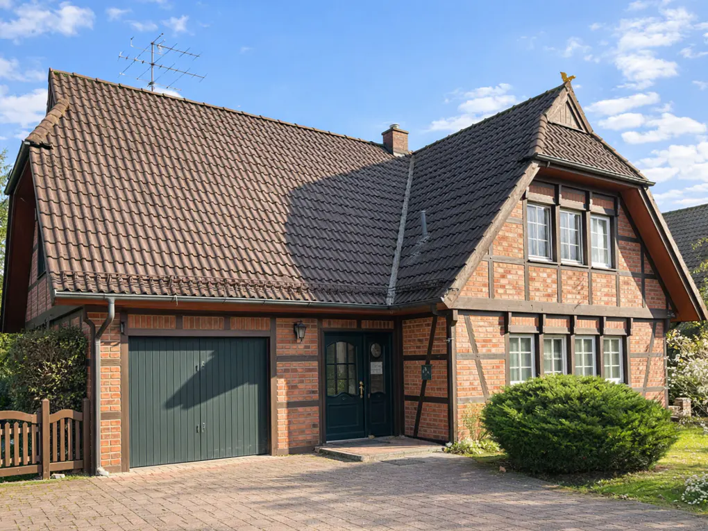 Two-story brick house with a brown tile roof, green garage door and front door, and a brick driveway.