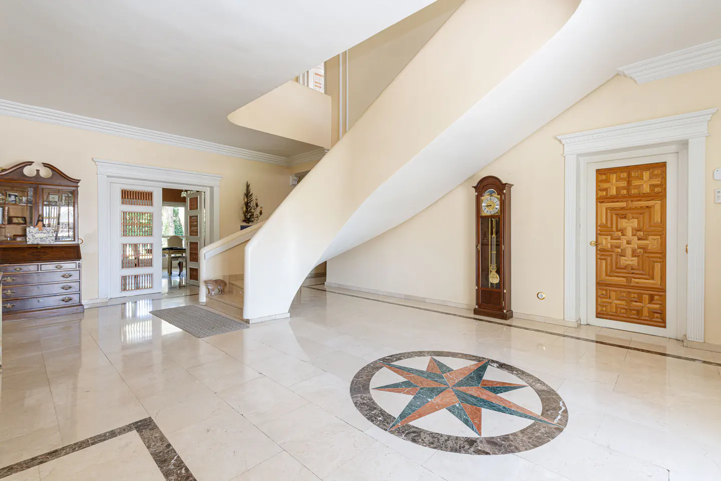 Bright foyer with marble floors, a compass design, and a winding staircase. A grandfather clock and a wooden door add character.