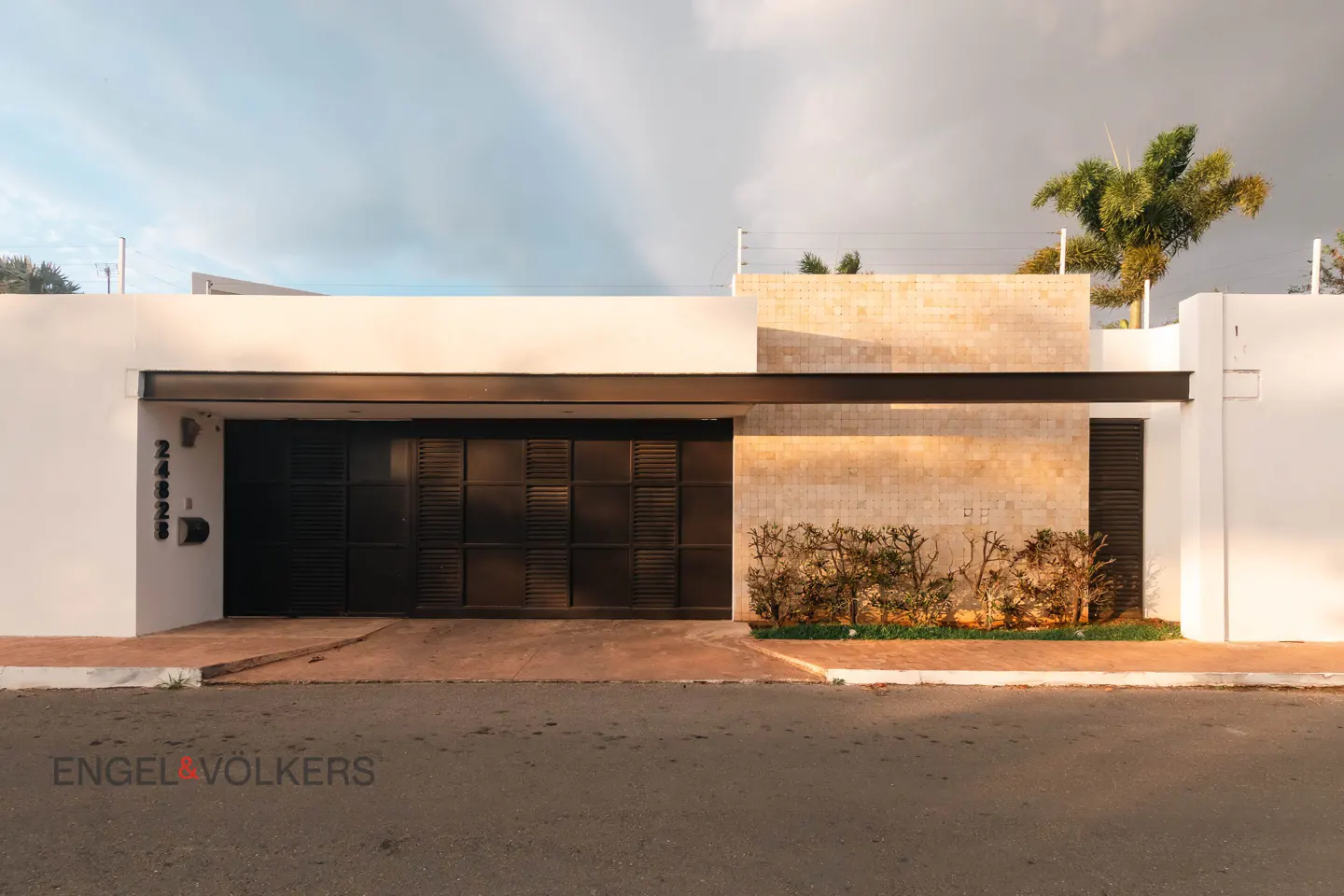 Modern home exterior with a black metal gate, white walls, and tan stone accents. A palm tree is visible in the background.