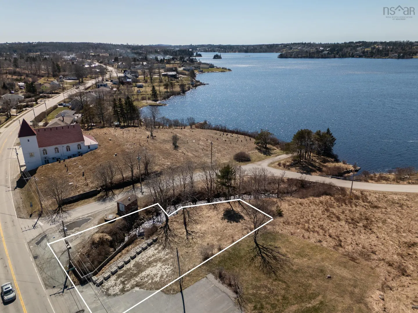 Aerial view of a vacant lot outlined in white, near a road, church, and lake on a sunny day.