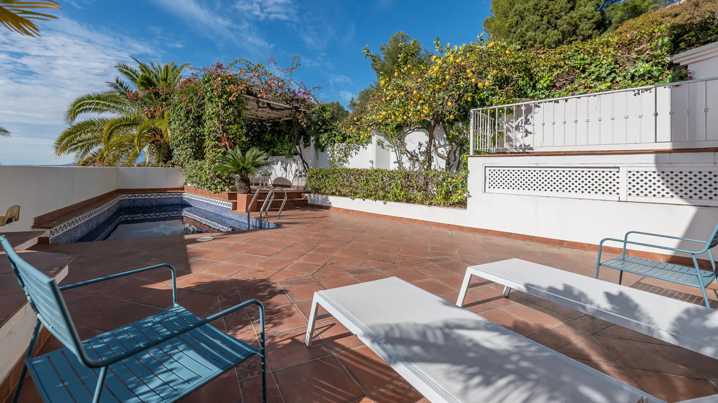Sunny terrace with a tiled floor, swimming pool, blue metal chairs, white lounge chairs, and lush lemon trees.