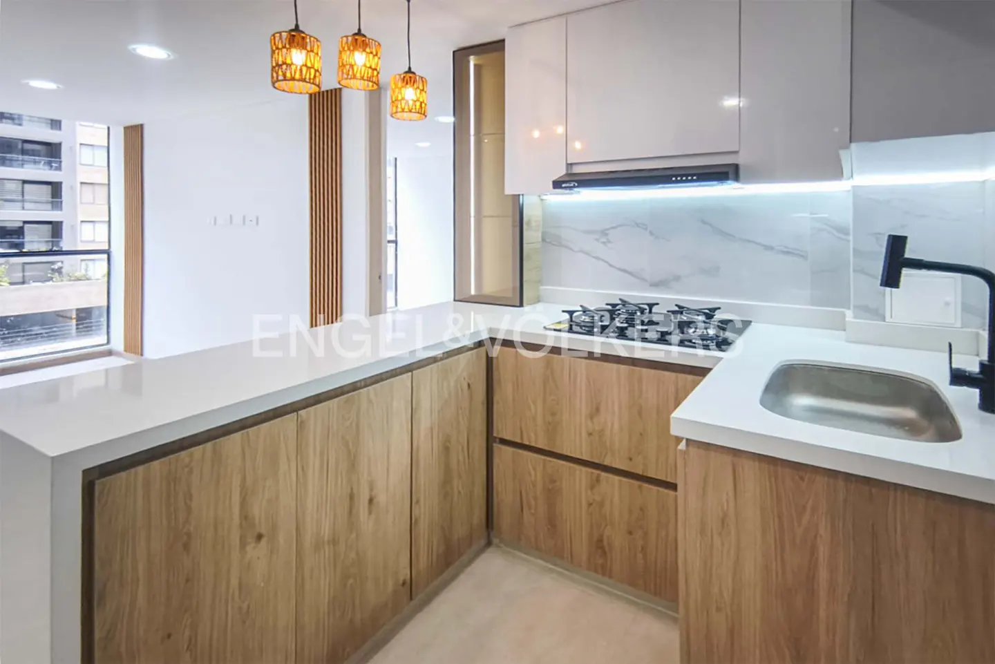 A modern kitchen with white cabinets, wood-grain lower cabinets, white countertops, and three orange pendant lights.