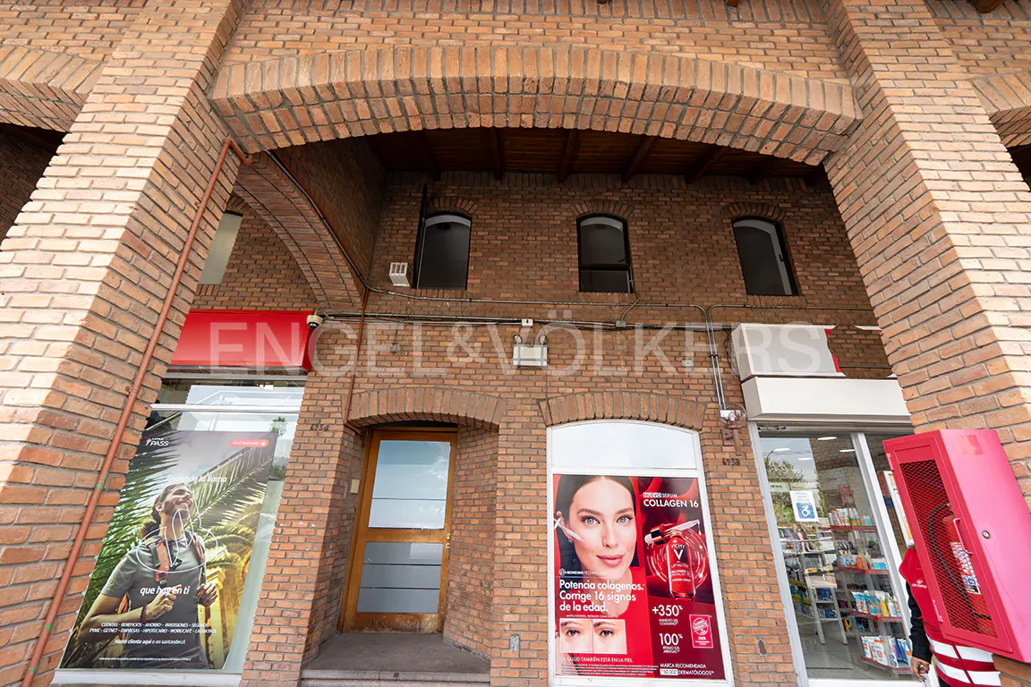 Brick building with arched entrances, windows, and storefronts. Posters are visible in the windows. An Engel & Völkers sign is above the storefronts.