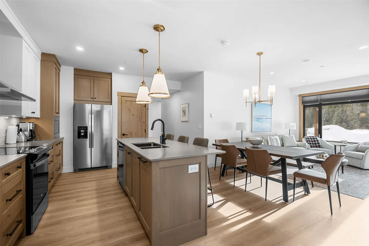 Open-concept kitchen and dining area with wood floors, island, stainless steel appliances, and view of snowy landscape.