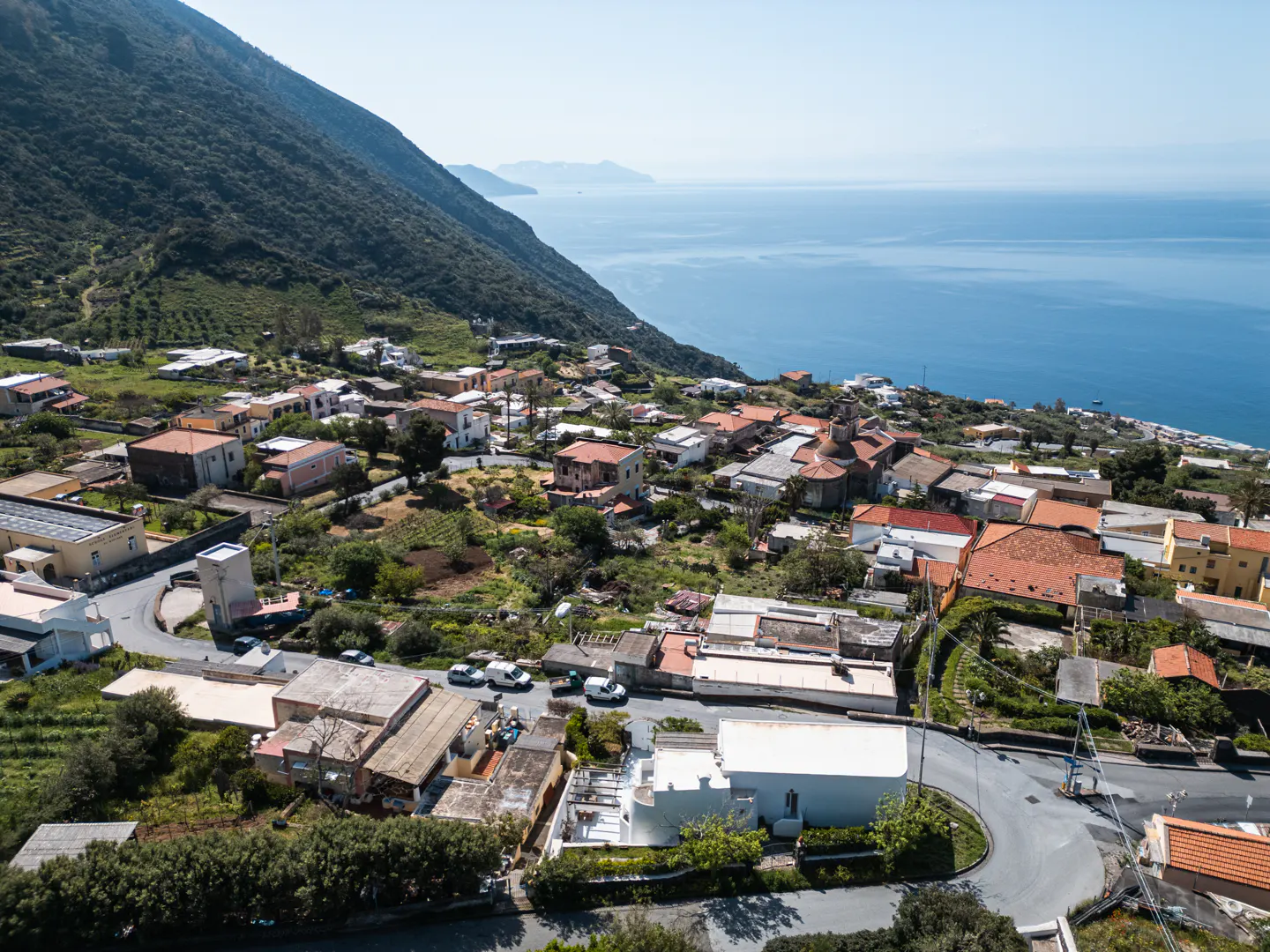 Aerial view of a coastal Italian village with red-roofed houses, a green mountain, and the blue sea.