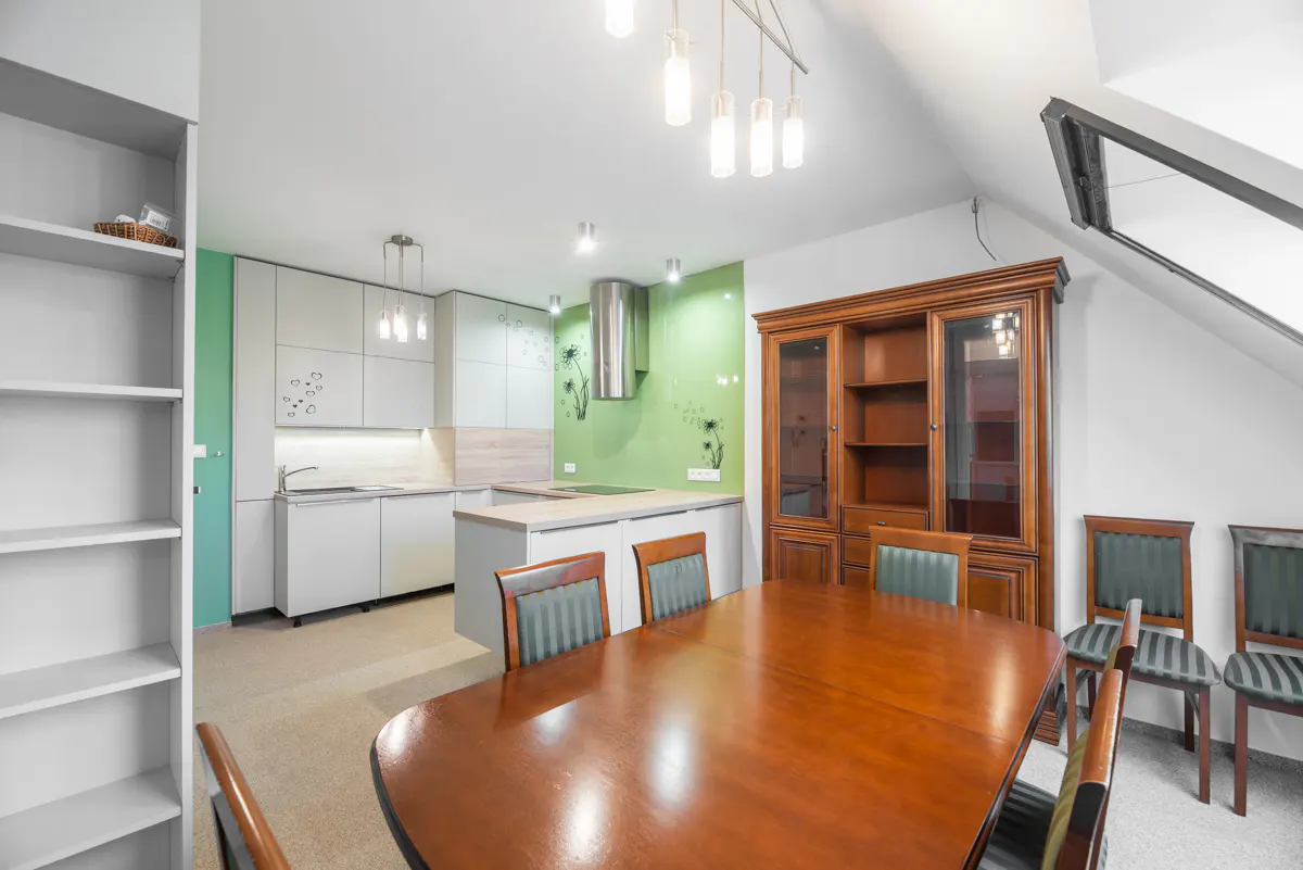 A bright kitchen and dining area with white cabinets, a wood table, and a brown hutch.