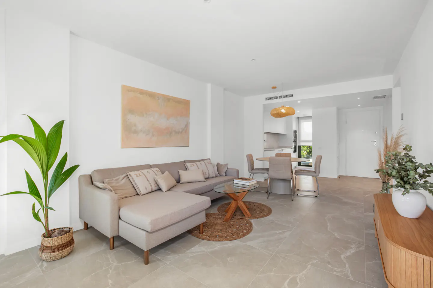 Bright living room with gray sectional sofa, round glass coffee table, and dining set. Neutral tones and modern decor.