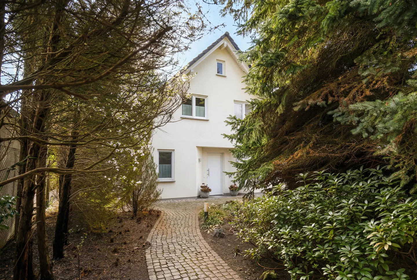 Two-story white house with a gray roof, surrounded by trees and bushes. A stone path leads to the white front door.