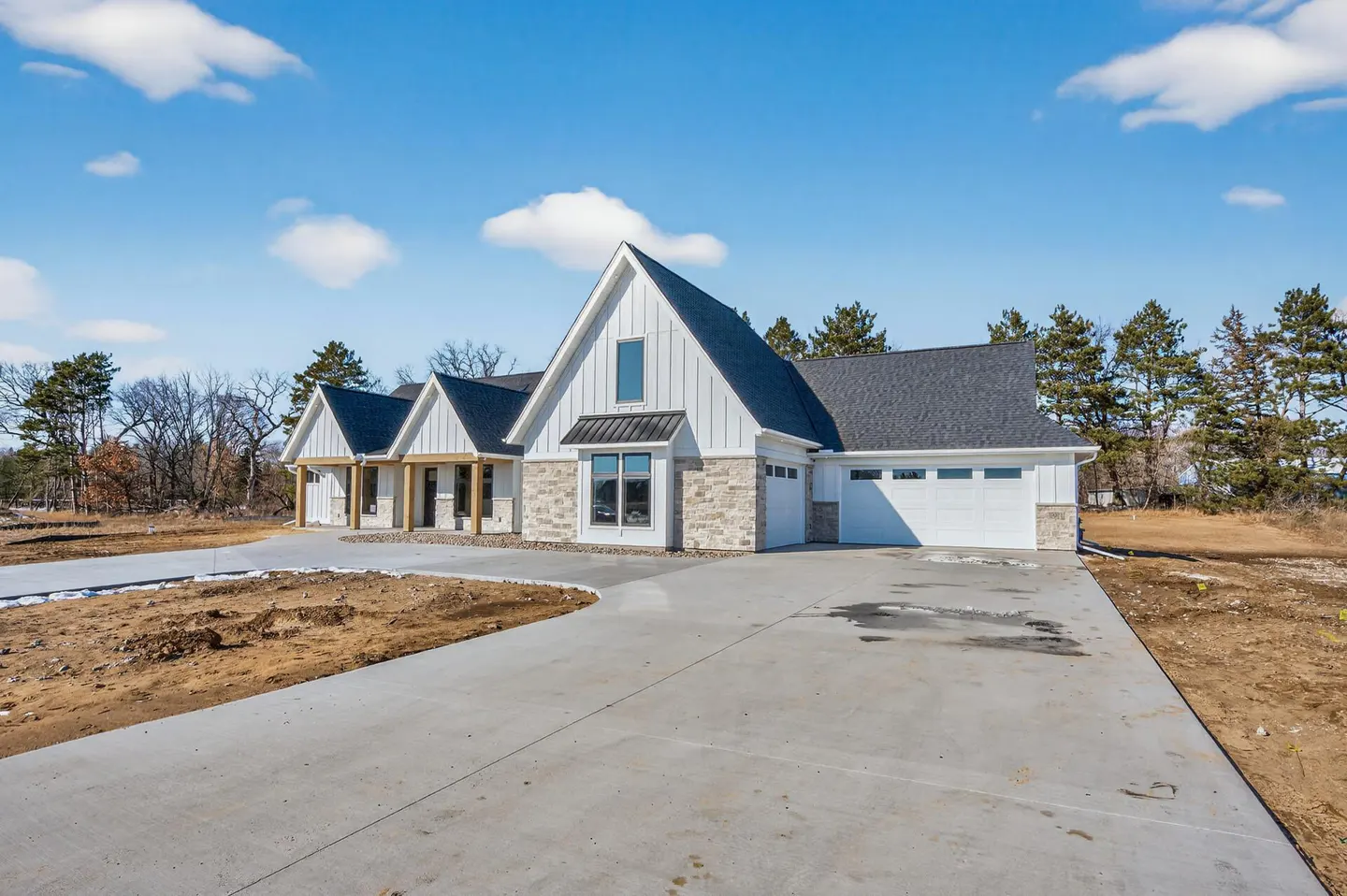 A modern, single-story home with white siding, stone accents, and a dark gray roof under a blue sky. A concrete driveway leads to a two-car garage.