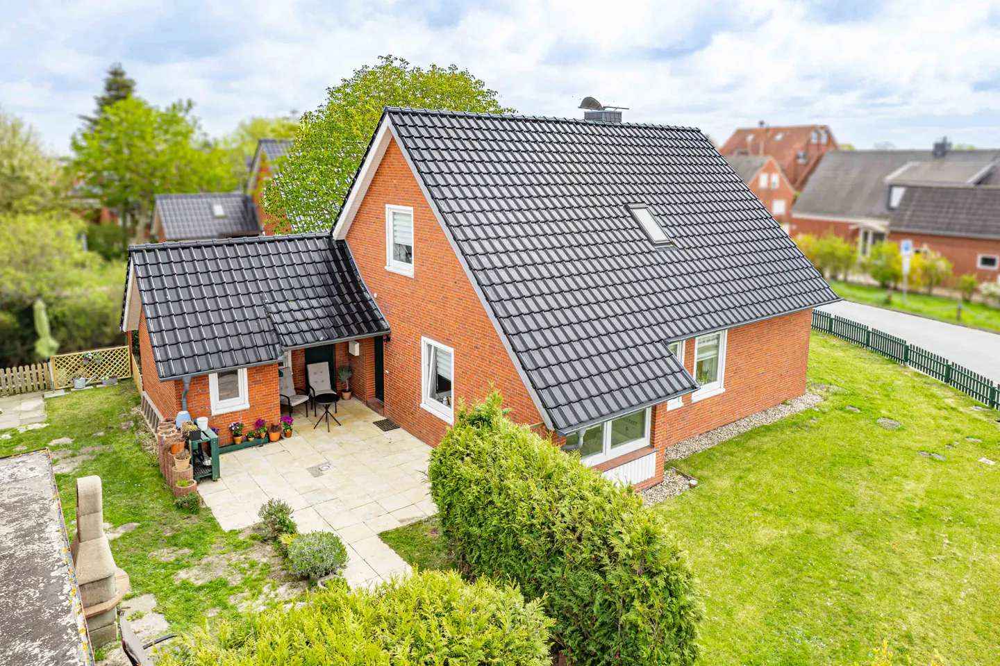 Aerial view of a red brick house with a black tiled roof, green lawn, and patio furniture.
