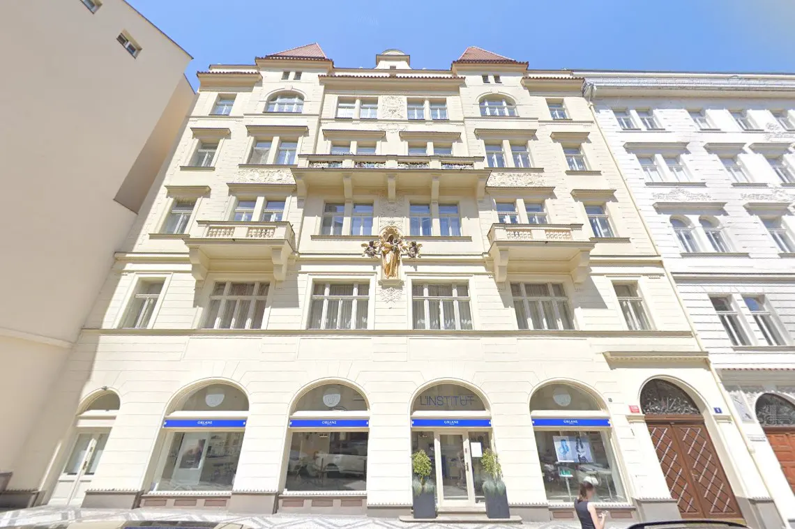 A light yellow, multi-story building with arched windows on the ground floor and a statue above.