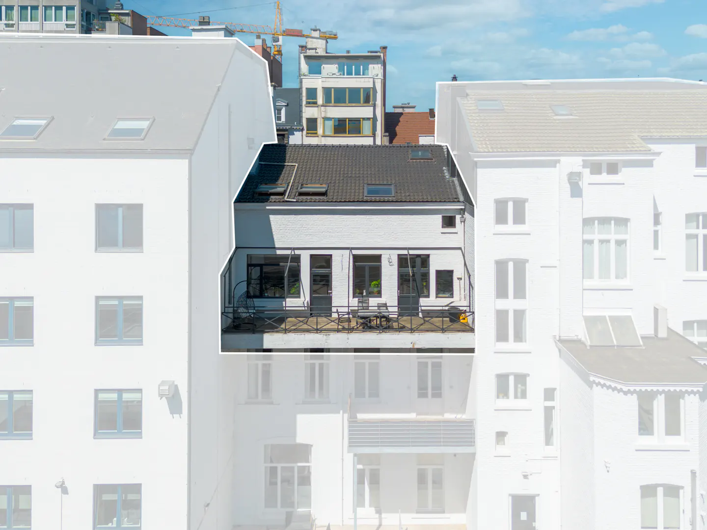 Exterior view of a white building with a dark roof and a balcony with furniture, surrounded by other buildings.