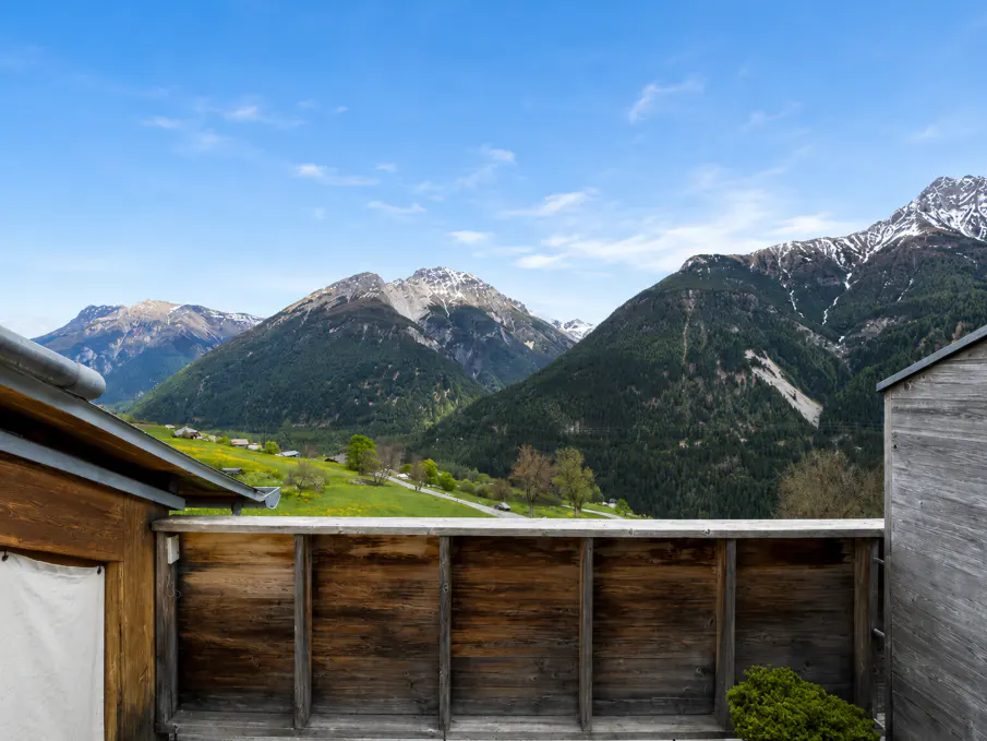 View from a wooden balcony overlooking green mountains and a blue sky.