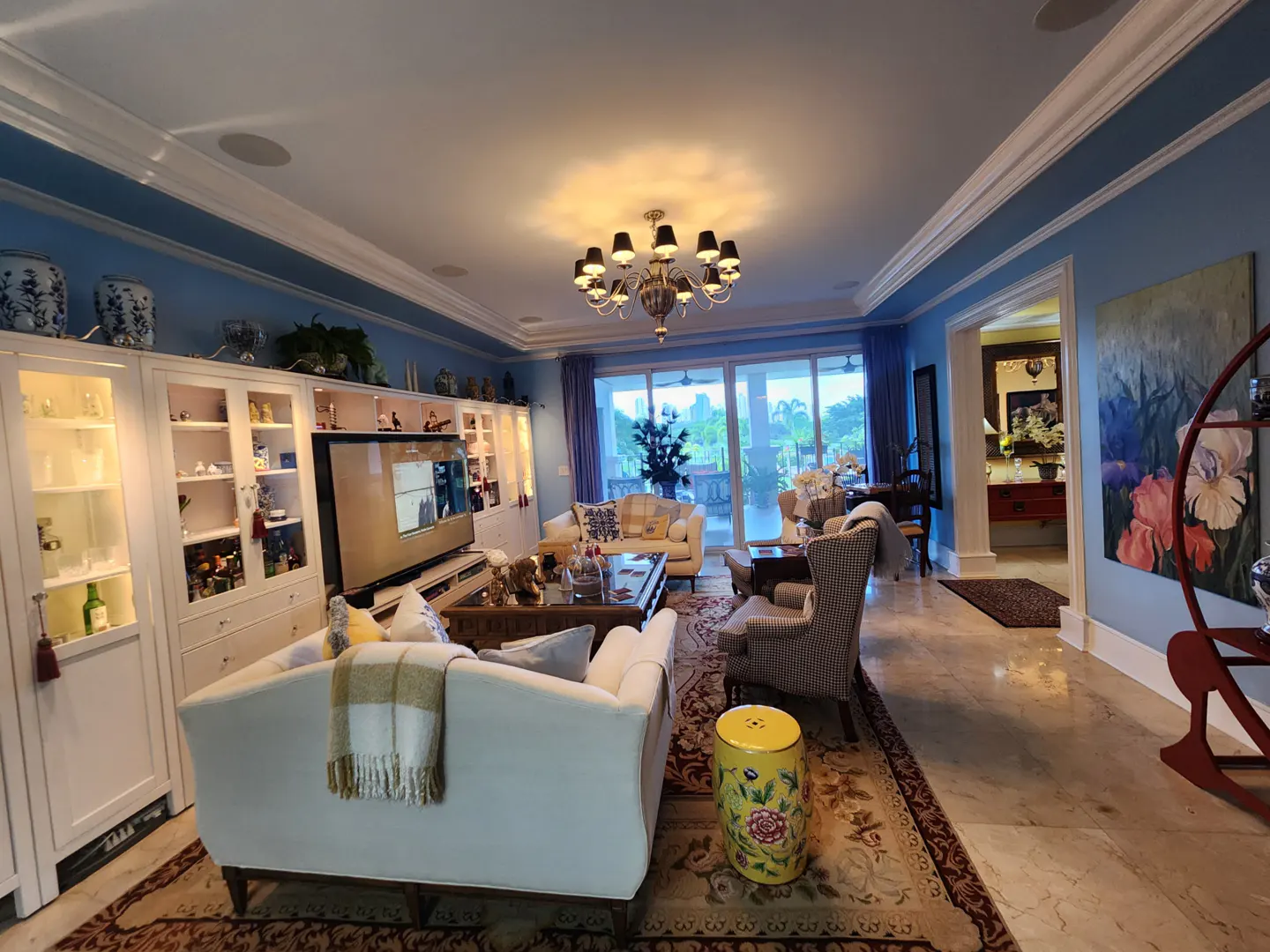 A wide shot of a living room with blue walls, white trim, and a chandelier. There are sofas, chairs, and built-in cabinets.