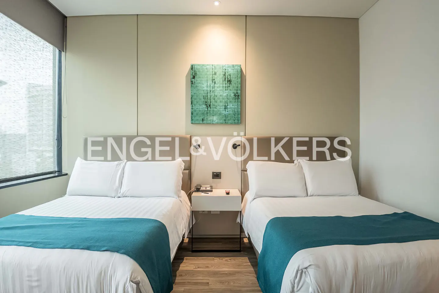 Bedroom with two beds, white linens, teal throws, and a headboard with "Engel & Völkers" logo. A green abstract art piece hangs above.