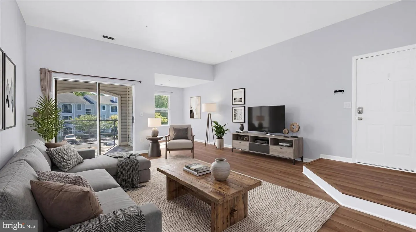 Living room with gray sofa, wood coffee table, TV, and white door. Balcony view of building.