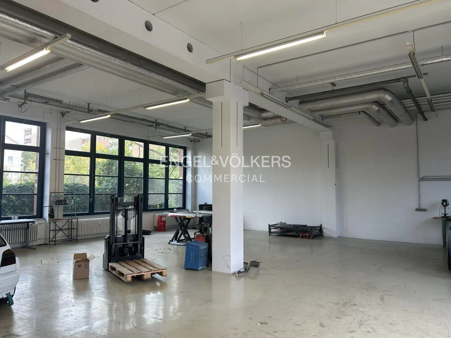 Bright, empty commercial space with a forklift, large windows, and Engel & Völkers logo on the wall.