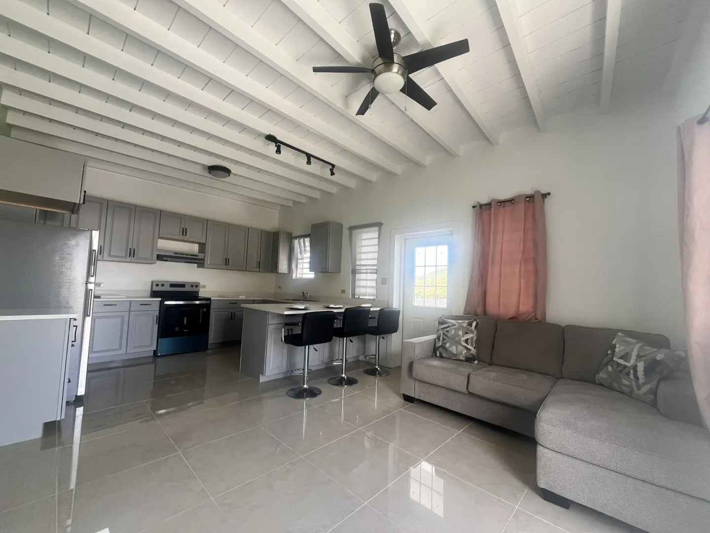 Open-concept living space with gray cabinets, island with stools, and a gray sectional sofa. White ceiling with a fan.