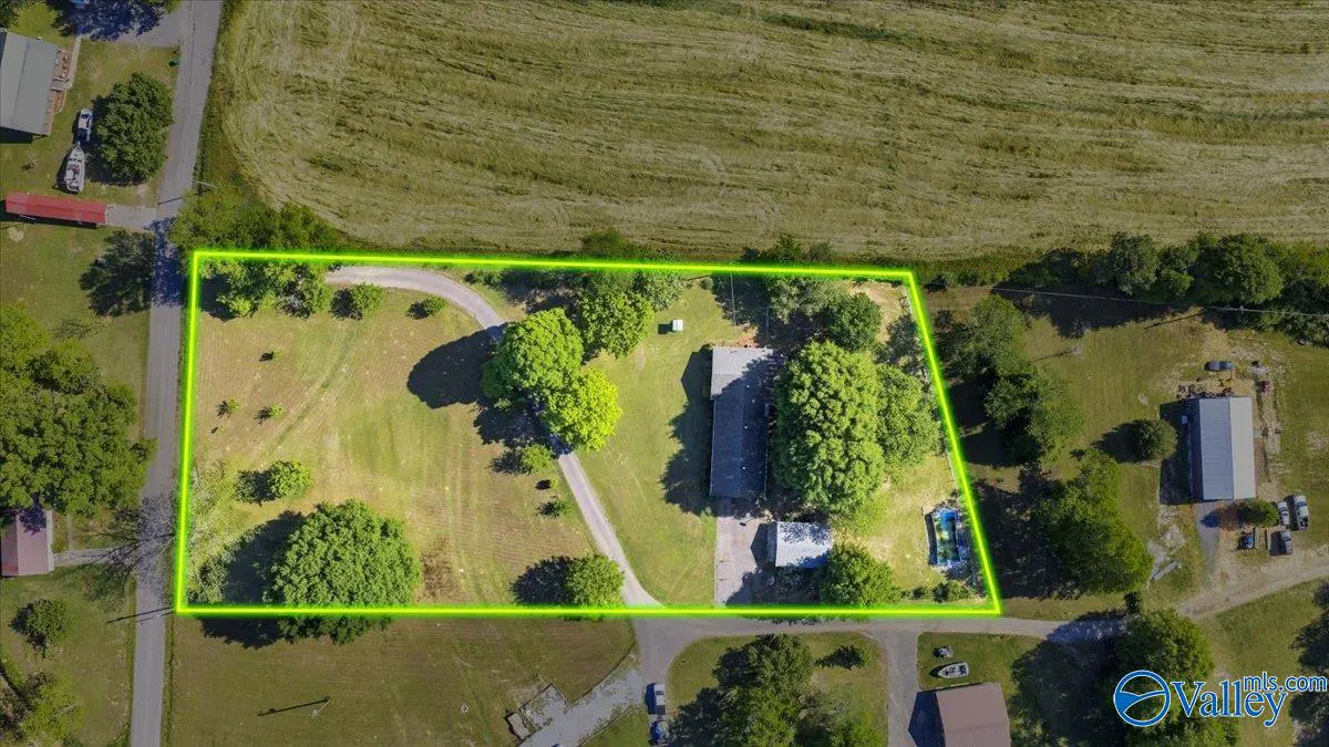Aerial view of a property with a house, trees, and a green border outlining the land. A driveway leads to the house.