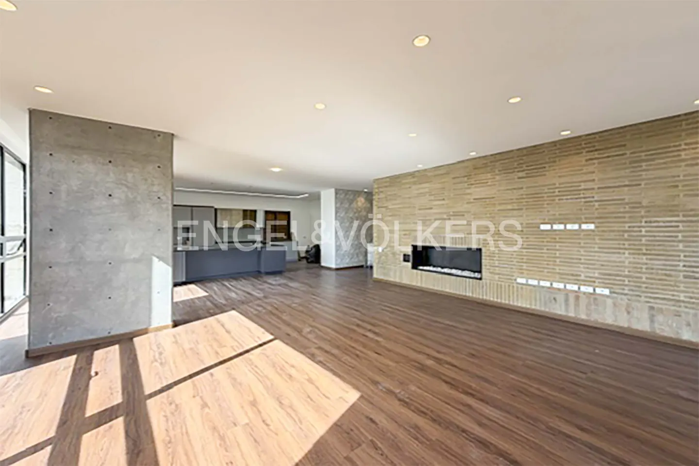 A wide shot of a modern living room with wood floors, a brick wall with a fireplace, and a gray kitchen island.