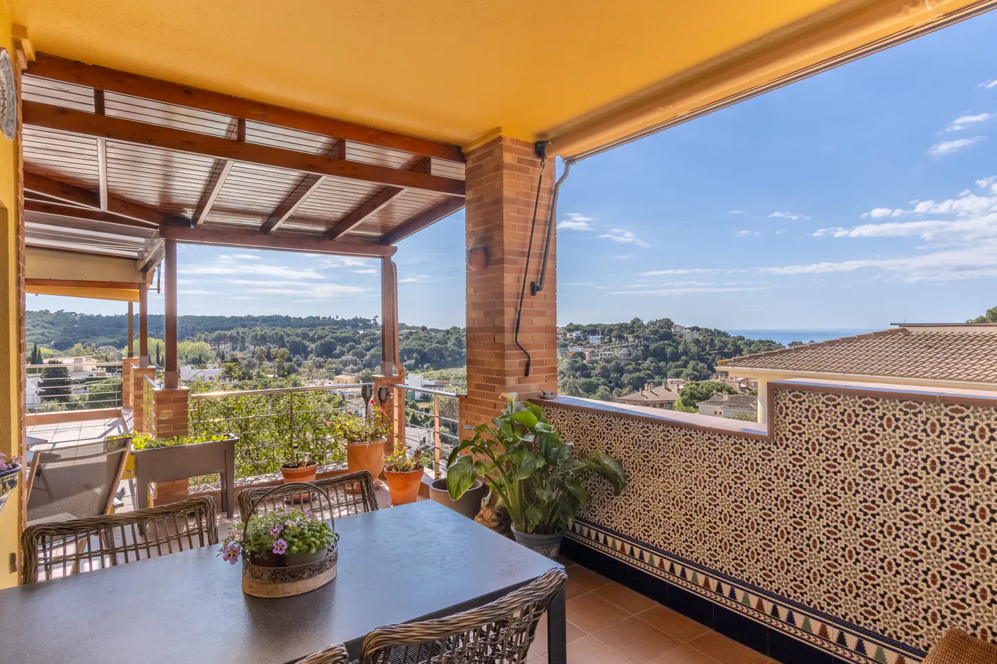 Outdoor patio with a table, chairs, and potted plants overlooking a green landscape and blue sky.