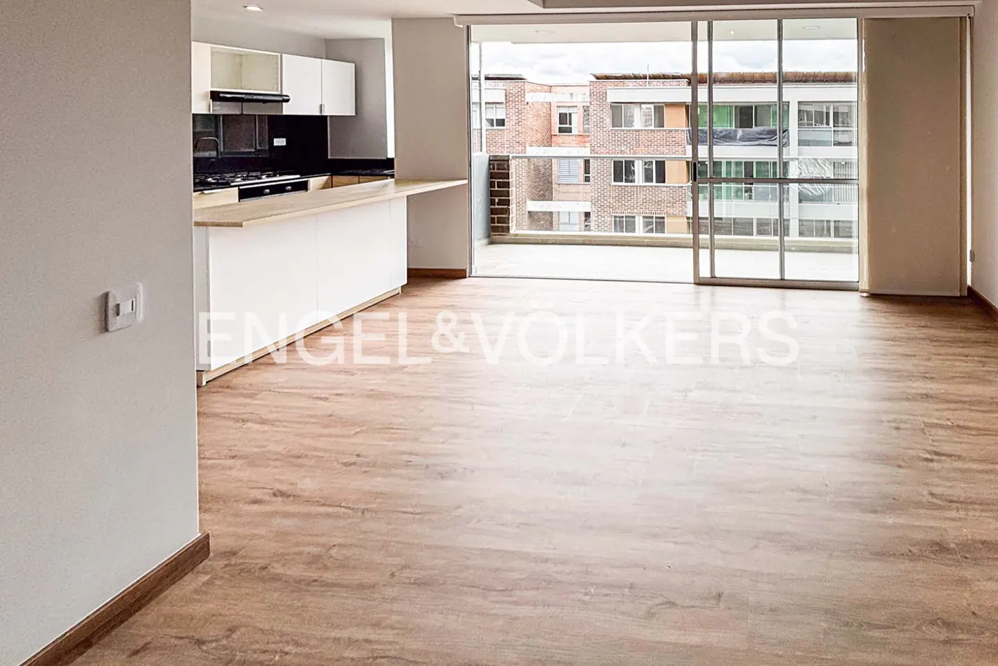 A bright, modern apartment with wood floors, a white kitchen, and a balcony with a city view.