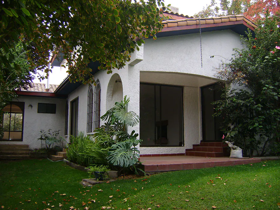 Exterior of a white stucco house with a red tile roof, surrounded by green lawn and lush foliage.